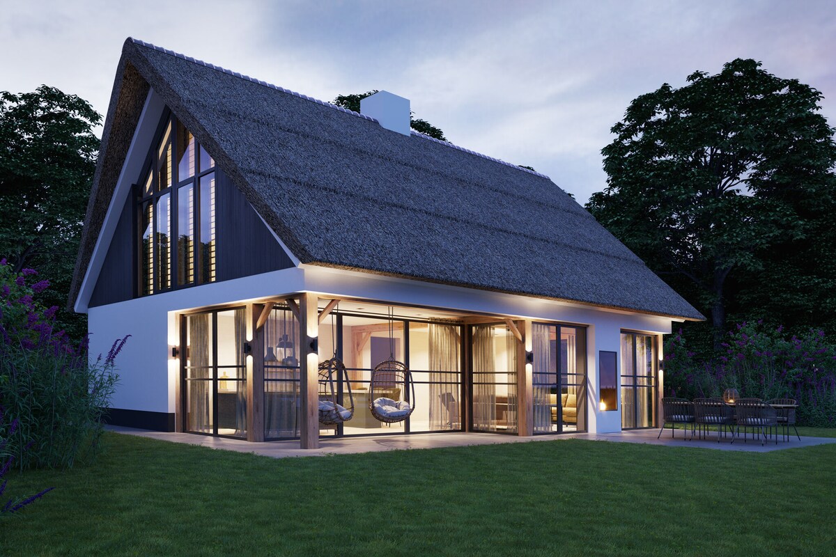 The villa features a thatched roof and large glass windows, allowing natural light to fill the interior. An outdoor terrace is visible with comfortable seating, surrounded by greenery. The landscaped garden creates a serene setting, enhancing the connection to nature.