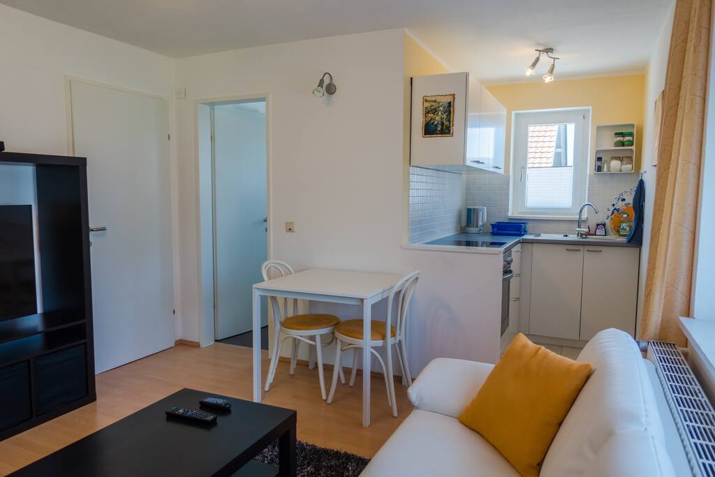 Living room, dining table and kitchen. Flat entrance between TV and bathroom door