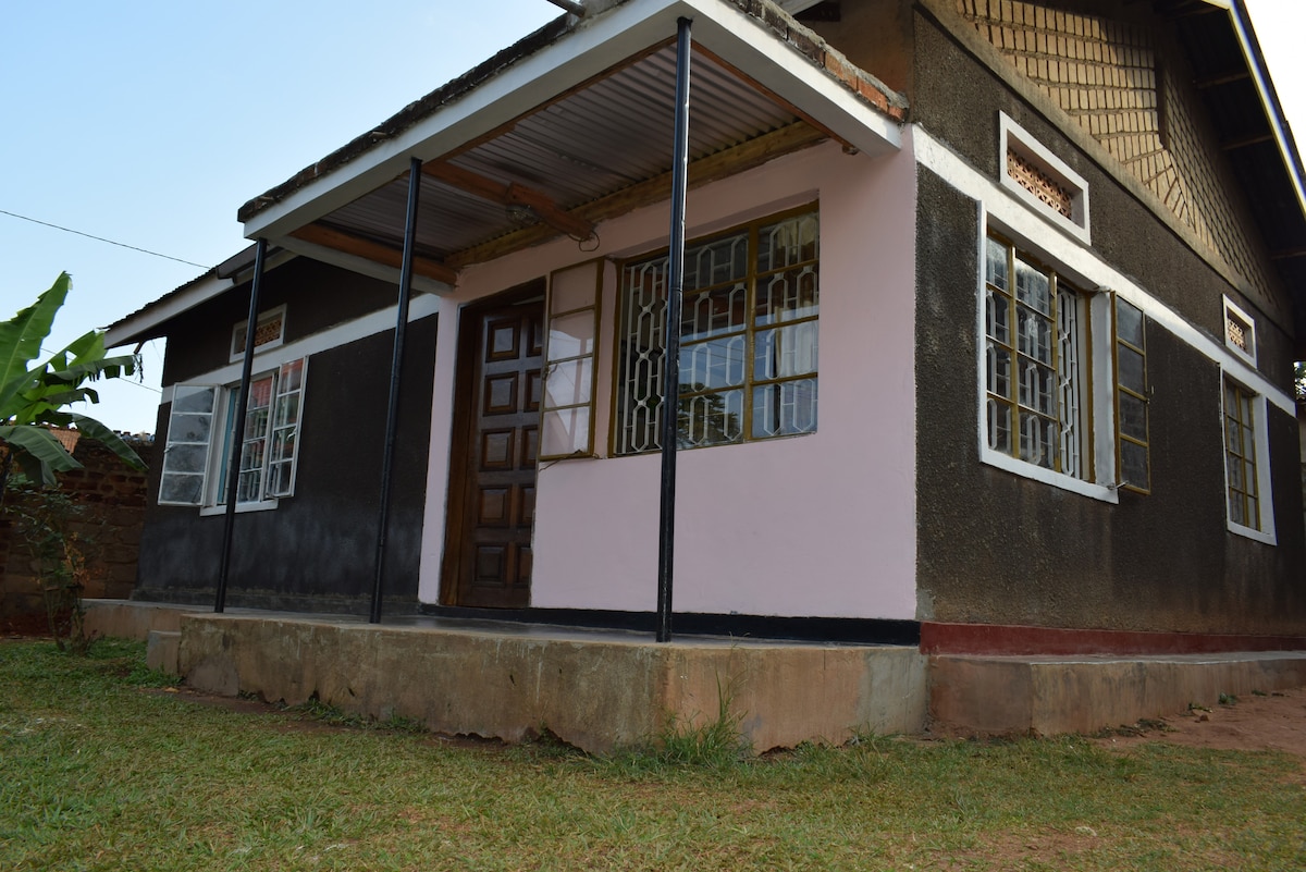 The bungalow features a covered porch with a metal roof, supported by black posts. Large windows provide natural light, with a combination of white and dark exterior walls. The grassy area in front adds to the home's inviting appearance.