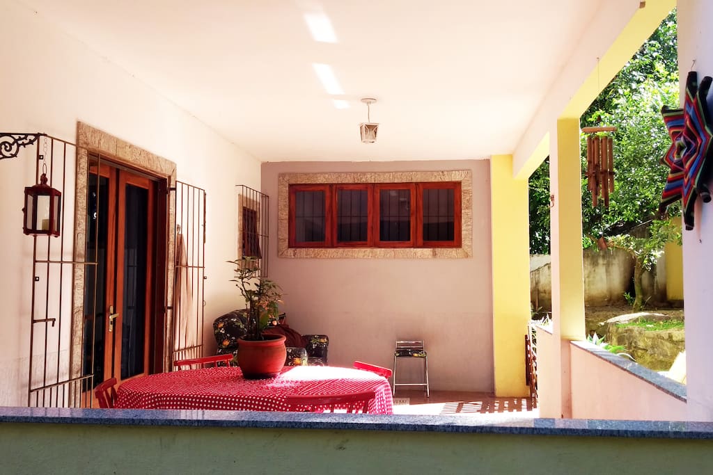 Varandinha com sol da manhã, rede, mesa e sofá.