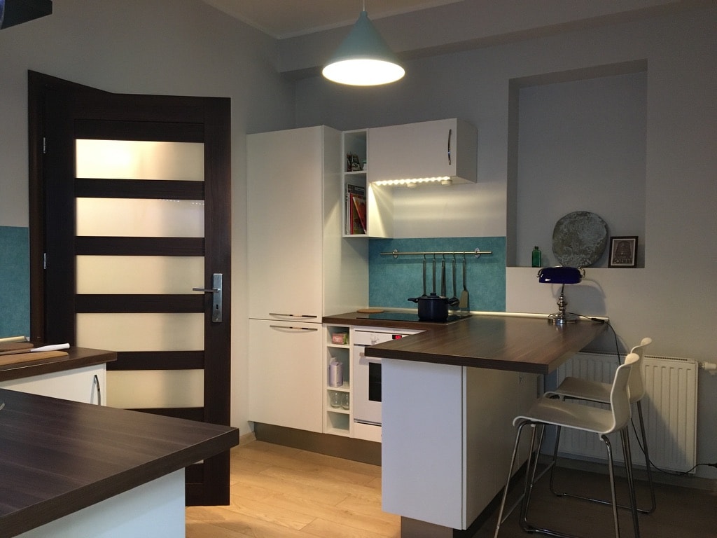 The kitchen features modern cabinetry with an induction hob and an integrated dishwasher. A wooden countertop provides workspace. A blue splashback adds a pop of color, while a pendant light illuminates the area. A radiator is positioned under the window.