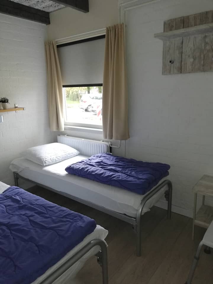 Chambre avec 2 lits simple et espace pour lit bébé.