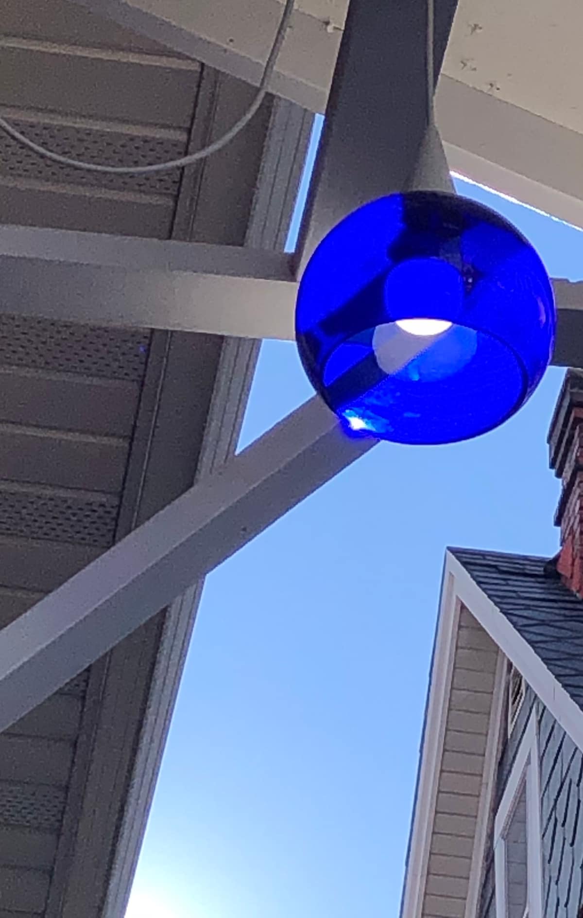 A uniquely designed blue pendant light hangs from a white ceiling beam. The clear sky is visible in the background, providing a bright contrast to the vibrant color of the light fixture.