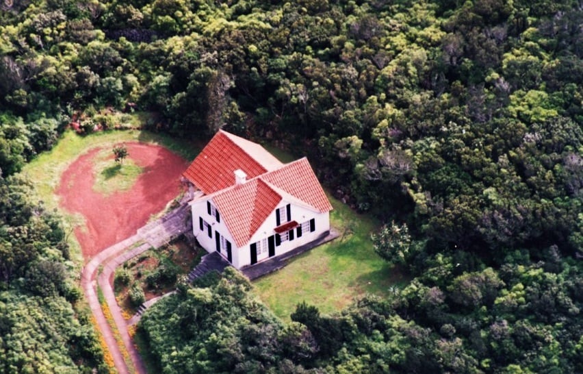 Aerial view of Casa do Areal, showcasing a charming two-story house surrounded by lush greenery. The red-tiled roof complements the white exterior, while winding paths lead to the home, set within a serene, natural landscape.