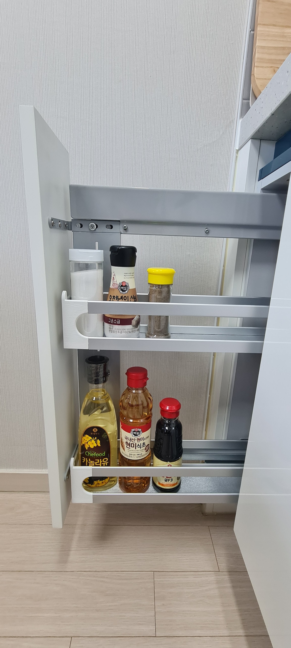 A pull-out storage unit displays various bottles, including oils and sauces. Two shelves hold six items, arranged neatly within the cabinet. The design promotes easy access, showcasing a clean and organized kitchen space.