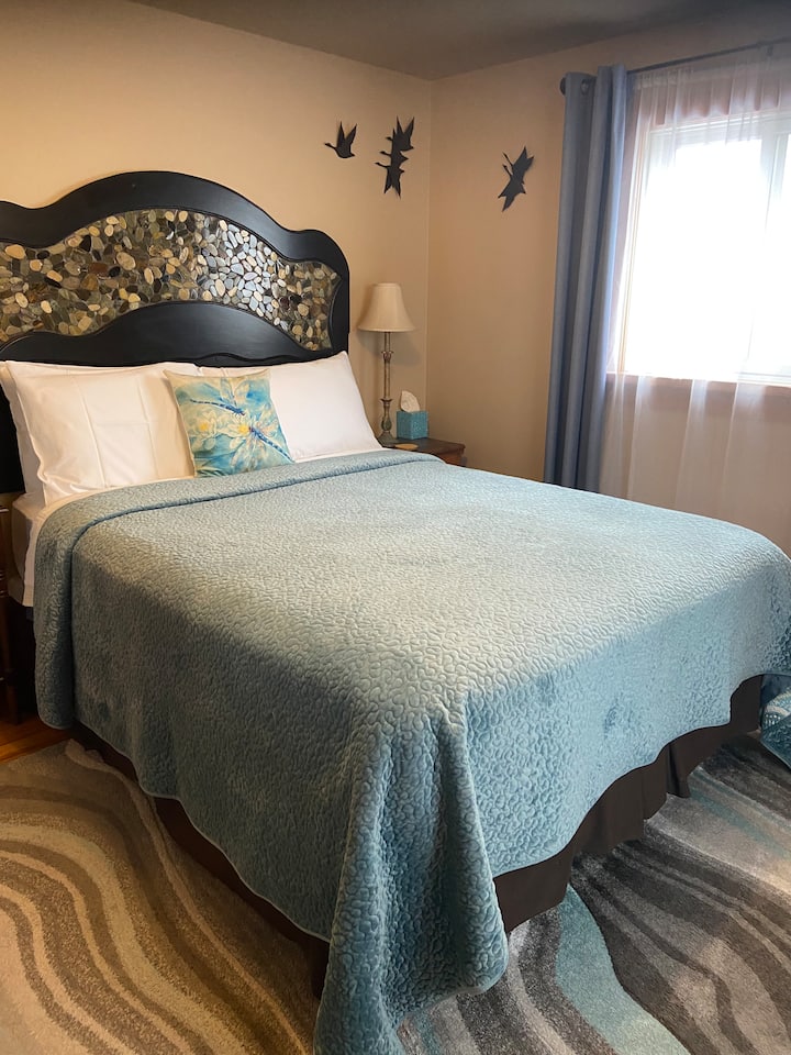 غرفة "نهر". سرير بحجم كوين مع طاولات جانبية وخزانة ومرآة وخزانة مع حامل أمتعة واحد وشماعات وكرسي صغير.