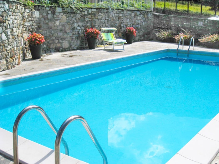 A shared pool is visible, featuring a clear blue surface and steps leading into the water. Surrounding the pool, potted flowers add color, while a green lounge chair is positioned nearby for relaxation.