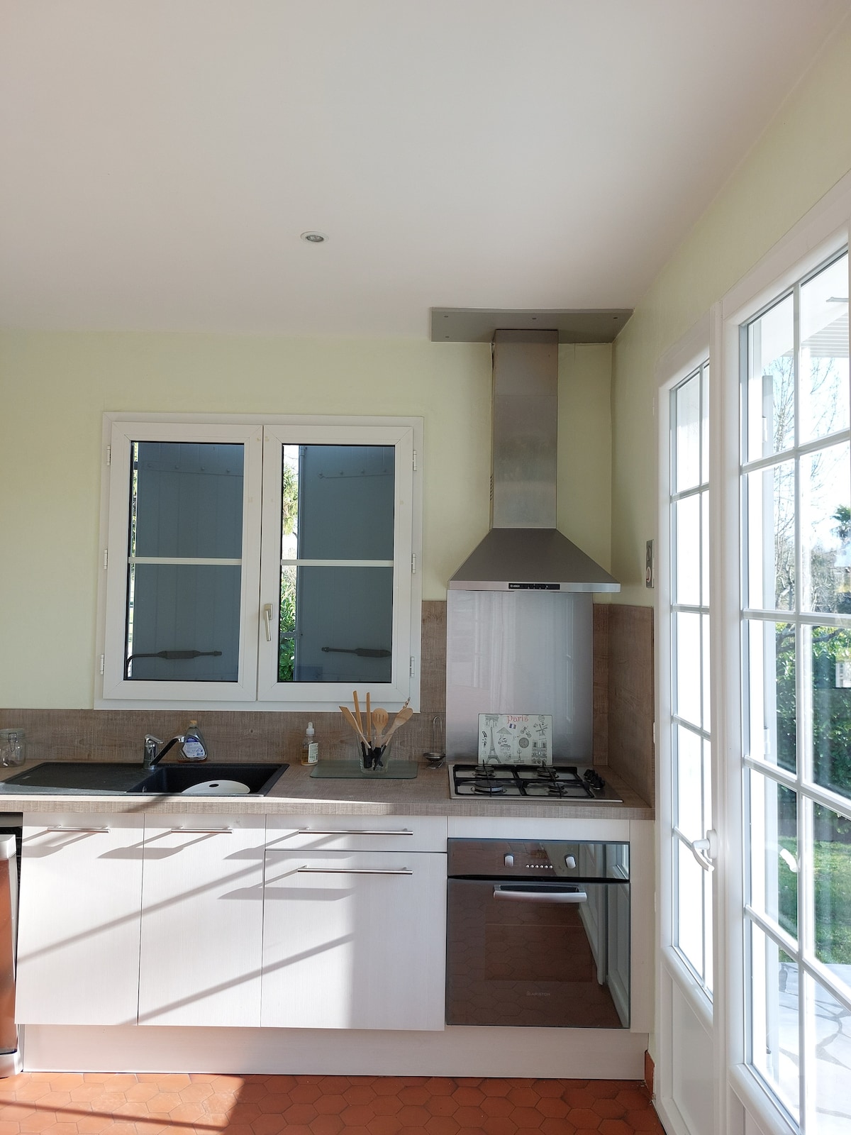 A well-equipped kitchen features modern appliances, including a gas stove and a stainless steel hood. Natural light fills the space through two windows, while cabinetry and countertops provide ample storage and workspace.