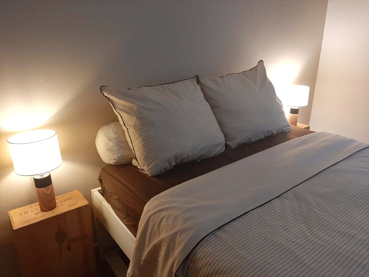 A cozy sleeping area is showcased with a spacious bed dressed in neutral linens. Soft lighting from two bedside lamps creates a calming ambiance. The adjacent nightstands add a touch of warmth, enhancing the overall tranquility.
