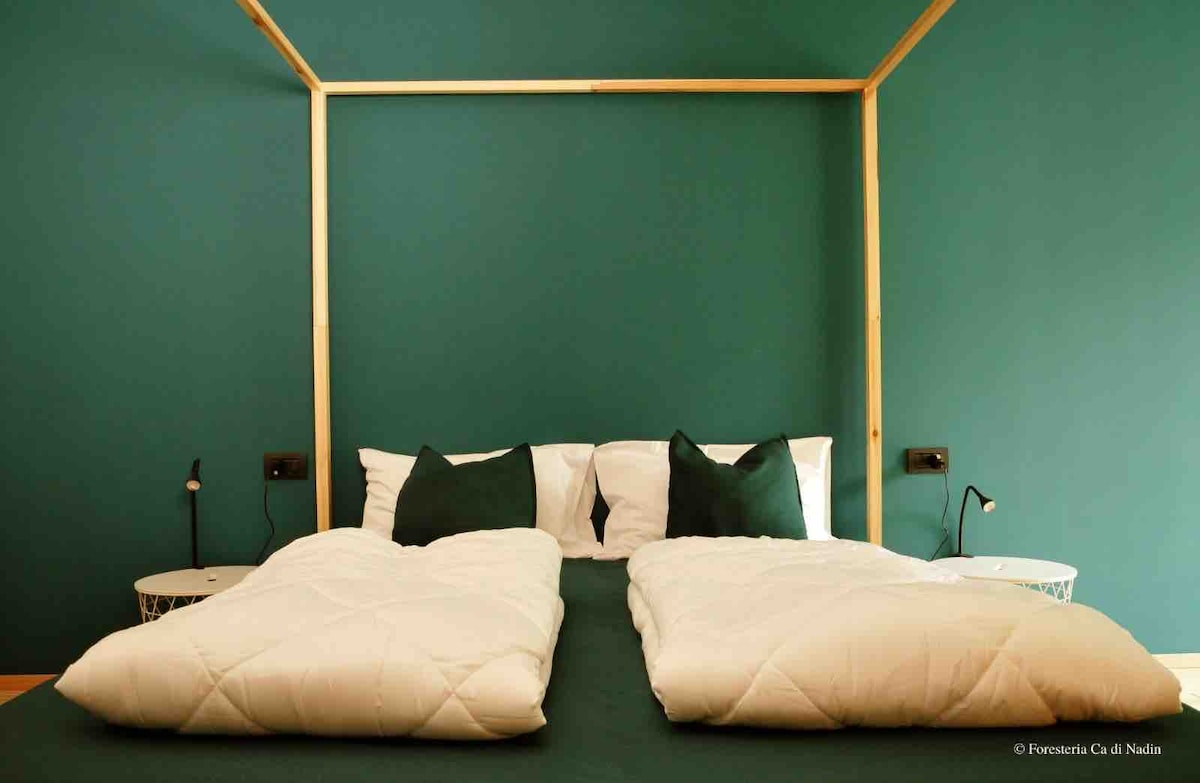 A spacious sleeping area features a four-poster bed adorned with crisp white linens and green accent pillows. The walls are painted in a soothing green hue, complementing the minimalist design of the bedside tables and reading lamps.