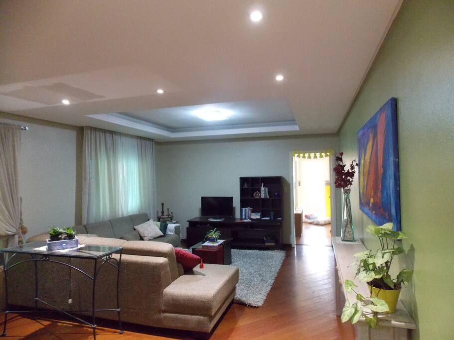 Vista da sala a partir da entrada do apartamento. TV de led, dvd, livros, revistas e folheteria da cidade.