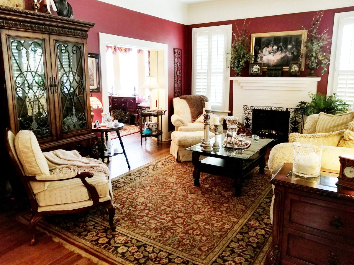 A cozy living area is presented, featuring a mix of elegant seating and decorative furnishings. A rich area rug covers the hardwood floor, and a traditional cabinet showcases decorative items. Soft lighting is provided by a lamp and the warm tones of the walls enhance the inviting setting.