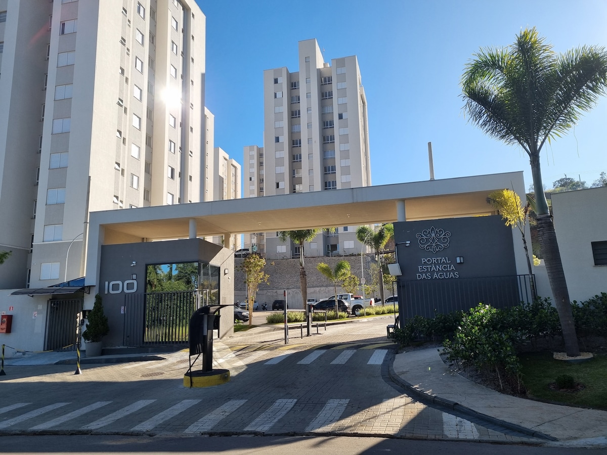 The entrance to the condominium is depicted, showcasing a contemporary building facade with a covered entryway. Tall palm trees are visible, complemented by well-kept landscaping. The surrounding area features a paved driveway leading to the entrance marked with the name of the property.
