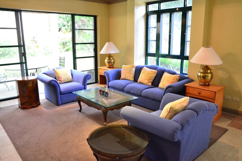 The spacious living room, with wooden flooring and comfortable couches, opens to the grassy lawn.