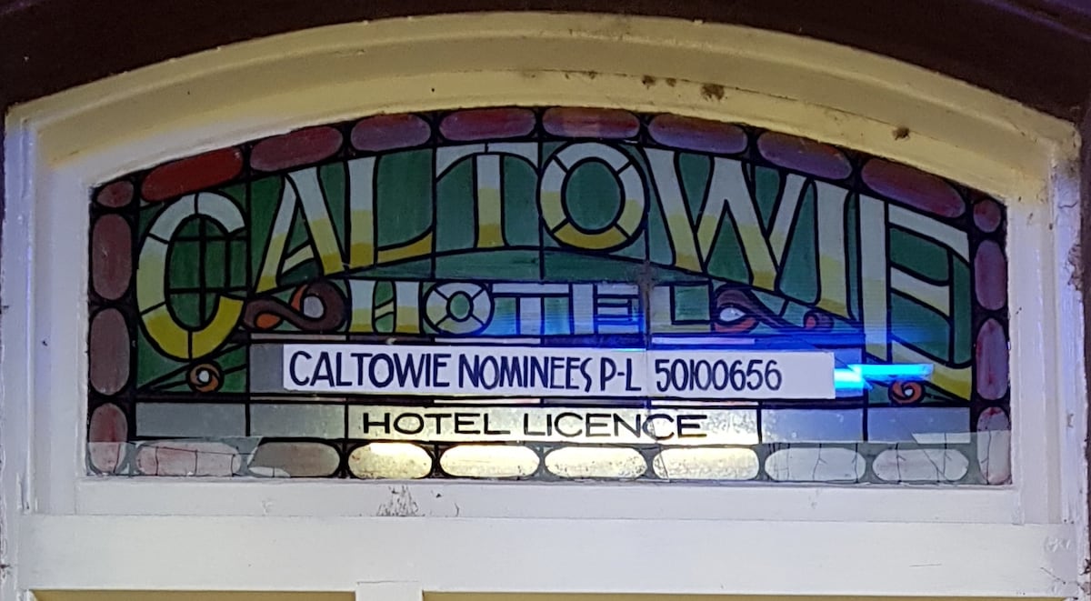 A stained glass sign featuring colorful lettering displays the name 'Caltowie Hotel.' The design incorporates an array of pastel colors, with the hotel's license number elegantly presented below in a contrasting white font.