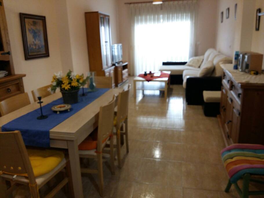 Amplio salón con balcón / terraza anexo. El cerramiento del balcón/terraza es doble, por lo que en el interior del salón la temperatura es muy estable todo el día. El salón dispone de sofá con chaise longue, una mesa centra y TV con TDT. También dispone de una mesa de comedor extensible y seis sillas así como muebles accesorios.