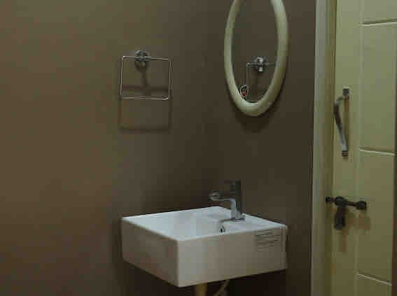 A compact bathroom space features a wall-mounted sink with a modern faucet. A round mirror is positioned above the sink, complemented by a towel rack on the wall. The neutral-colored walls provide a simple backdrop, and a door is visible on the right side.