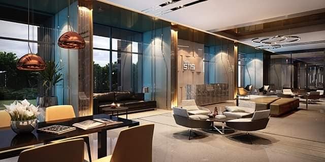 An open-plan living and dining area is seen, featuring modern furnishings in neutral tones. A sleek dining table is accompanied by four chairs. Contemporary pendant lights hang above the space, which is illuminated by large windows offering views of greenery.
