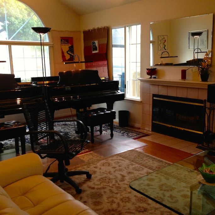Living room with cathedral ceiling, two grand pianos, leather reclining sofas, and fireplace
