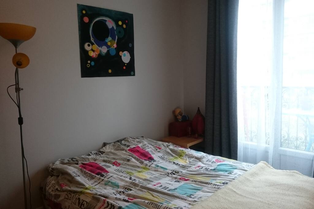 Chambre confortable avec un grand lit, une armoire avec portes vitrées, des hautes fenêtres donnant sur un balcon