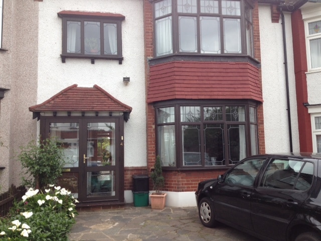 The exterior of the home displays a two-story structure with a prominent bay window and a covered entryway. Flowering plants are positioned beside the entrance, and a small vehicle is parked on the stone pathway, adding to the inviting appearance of the residence.