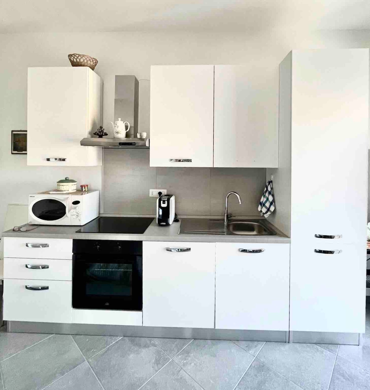 A modern kitchen setup features sleek white cabinetry and stainless steel appliances. A microwave, coffee maker, and oven are prominently displayed. The kitchen area is well-lit, showcasing a clean and functional design suitable for meal preparation.