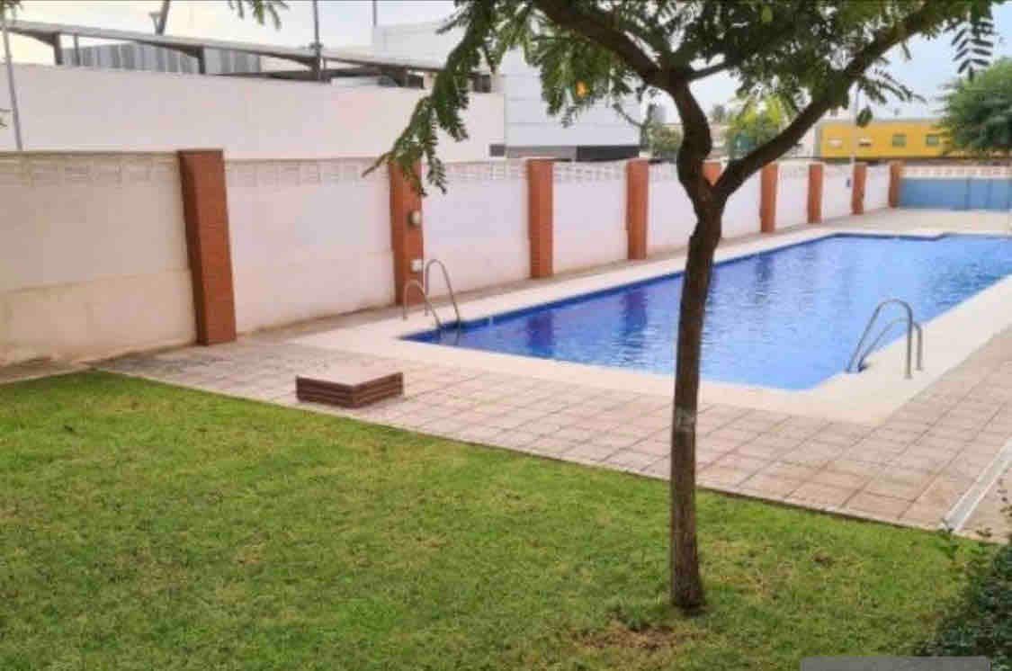 A well-maintained swimming pool is surrounded by tiled decking and a neatly trimmed lawn. The pool features two sets of stairs for easy access. A young tree provides some shade along one side of the area, contributing to a serene environment.