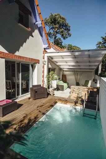 A private outdoor area showcases a mini pool alongside a wooden deck. Comfortable seating options are visible under a shaded patio, surrounded by greenery. The entrance to the studio is seen through expansive sliding glass doors, enhancing the connection to nature.