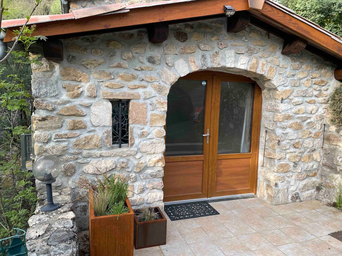 The entrance features a wooden door framed by a stone archway. A small window is visible to the side, and potted plants are placed near the entrance. Natural stone tiles cover the entryway, complemented by a welcome mat.