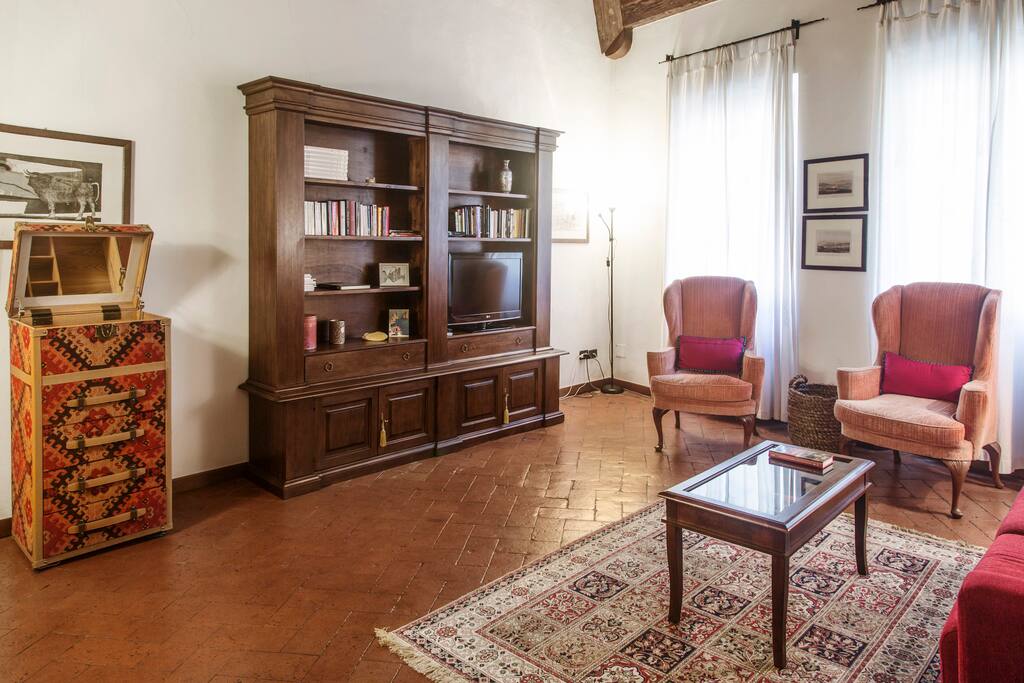 Spacious high ceiling living room, furnished with a mix of classical and modern furnitures. The floor is traditional "cotto fiorentino" (Florentine fired brick). Plenty of light comes from two large windows facing the main road
