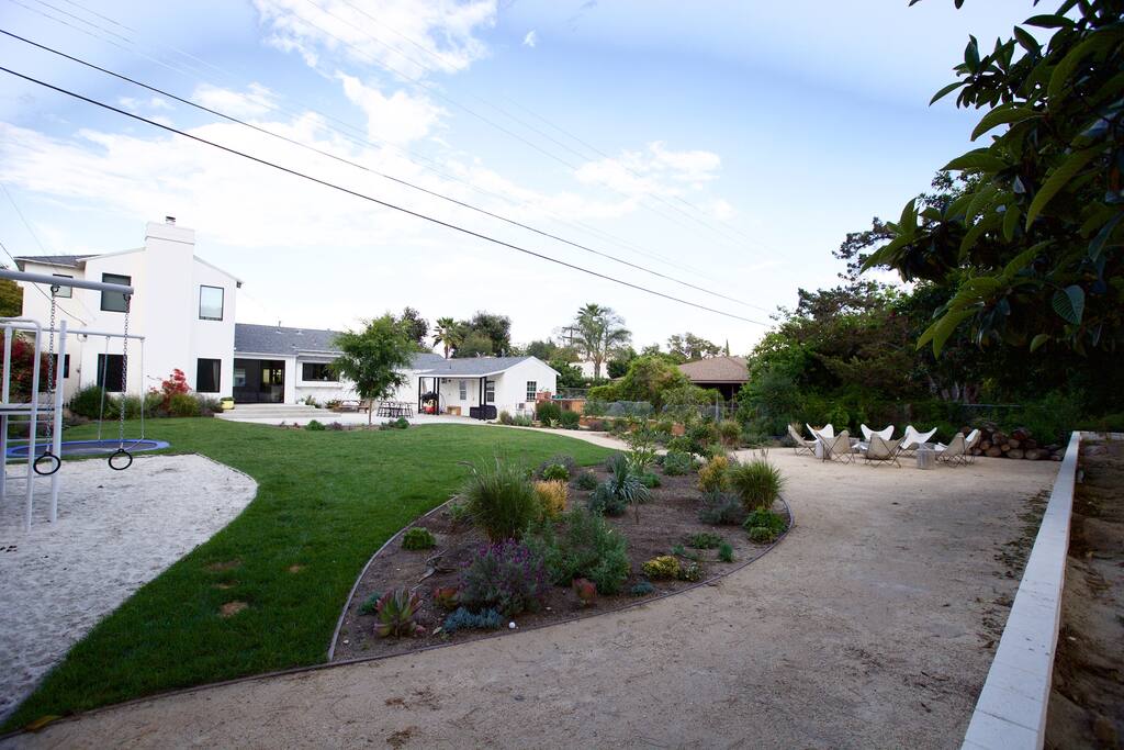 The backyard has a kid play structure with swings and a slide and an in ground trampoline.