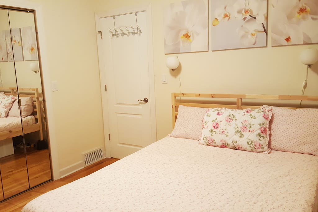 The "Floral Bedroom" has 1 queen bed, mirrored closet doors, closet access, luggage rack, 2 bedside tables with drawers, two wall lamps, and a hair dryer- all ready for guest use.