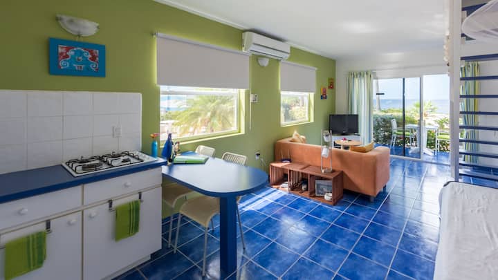 ห้องนั่งเล่นตกแต่งอย่างมีสีสันหน้าต่างและประตูบานเลื่อนมีมุ้งลวดมีเครื่องปรับอากาศและพัดลมติดผนัง ใต้บันไดมีเตียงสำหรับวันหยุด 2 เตียง (พร้อมมุ้งกันยุง) และตู้เสื้อผ้า