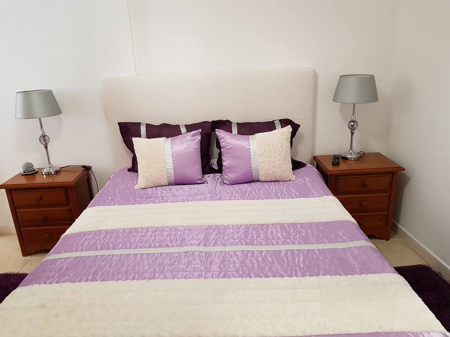 Quarto com cama de casal, TV, mesas de cabeceira, candeeiros, poltrona e roupeiro