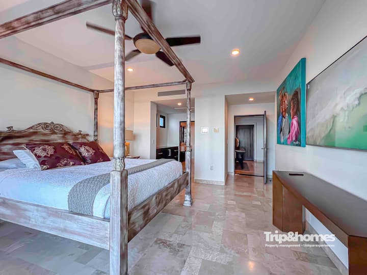 Dormitorio principal en planta baja con cama tamaño queen, baño privado, televisión, vista a la playa y armario.