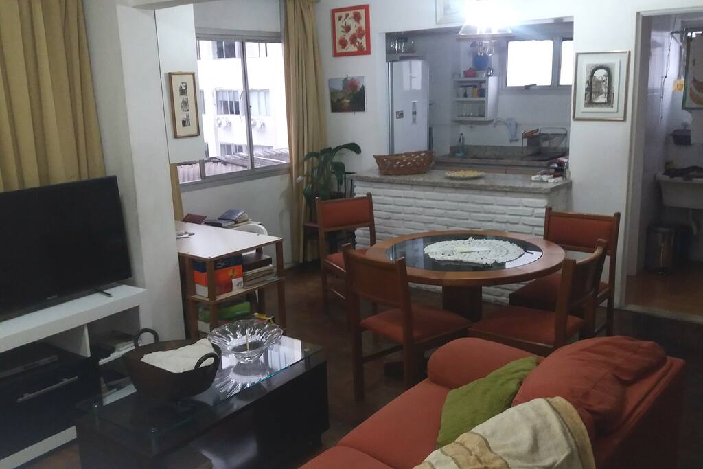 Sala de estar e jantar com mesa de trabalho e cozinha americana.