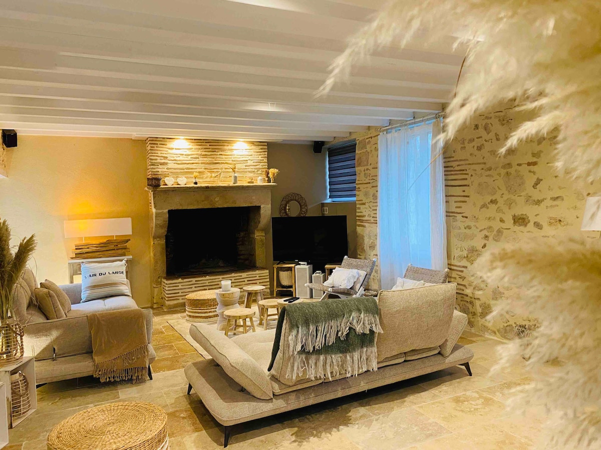 A spacious living area features a cozy seating arrangement with a light-colored couch and armchairs. The stone fireplace is a central focus, complemented by warm lighting. Decorative elements like a side table and plants enhance the inviting atmosphere.