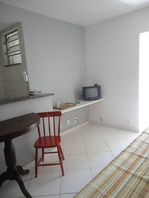 Foto da sala com mesa redonda e cadeiras, rack com TV ventilador de teto e sofá cama.