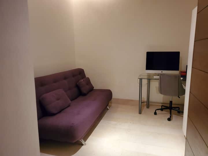 Estudio con sofá cama, guarda ropa,  escritorio con computadora y silla 