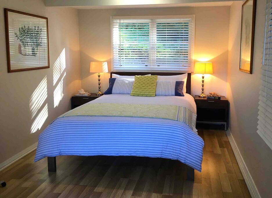 Queen bed and bedside tables and lamps with rear window facing onto rear of Bouddi National Park