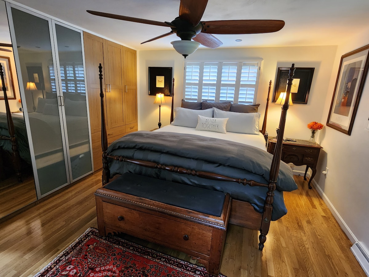 Suite du propriétaire : LIT KING BEAUTY REST BLACK SERIES, placard, ventilateur de plafond, bois franc, téléviseur LG 55", salle de bain privée avec douche à l'italienne, siège rabattable en teck, meuble-lavabo avec comptoir en granit, armoire de médicaments avec miroir, carrelage en granit, détail de mur en bois à planches et lattes.