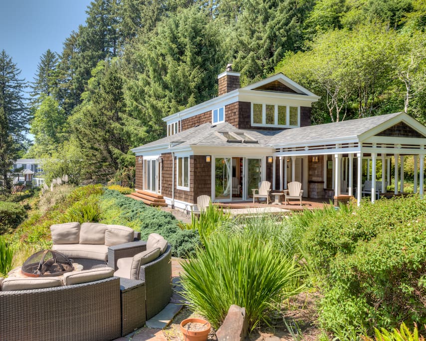 Side view of Maison de la Lune with a beautifully landscaped yard, stone patio with fire pit, ocean facing deck with patio furniture and covered entry.