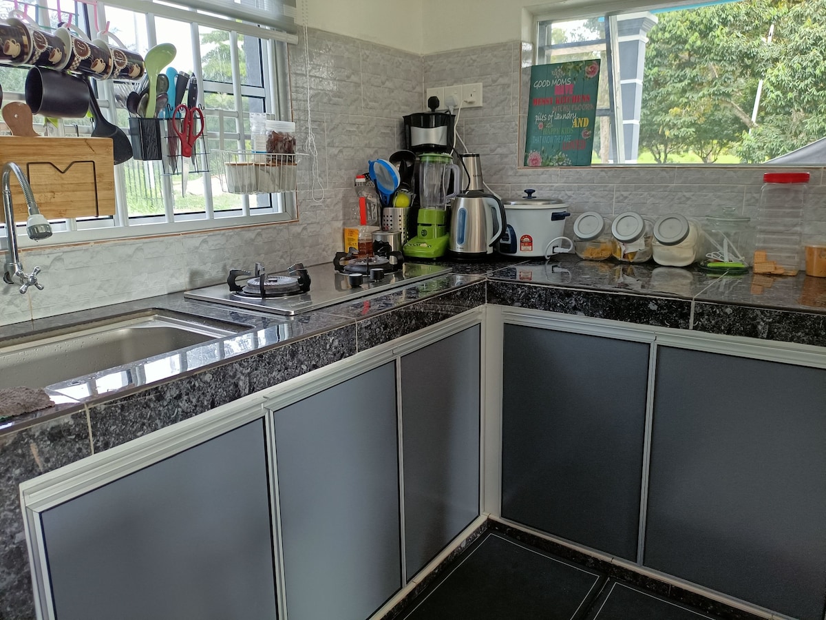 A functional kitchen corner features a gas stove, a countertop with various small appliances, and a sink. Kitchen tools are neatly organized on a hanging rack, while containers and utensils are arranged on the countertop, offering convenience for meal preparation.