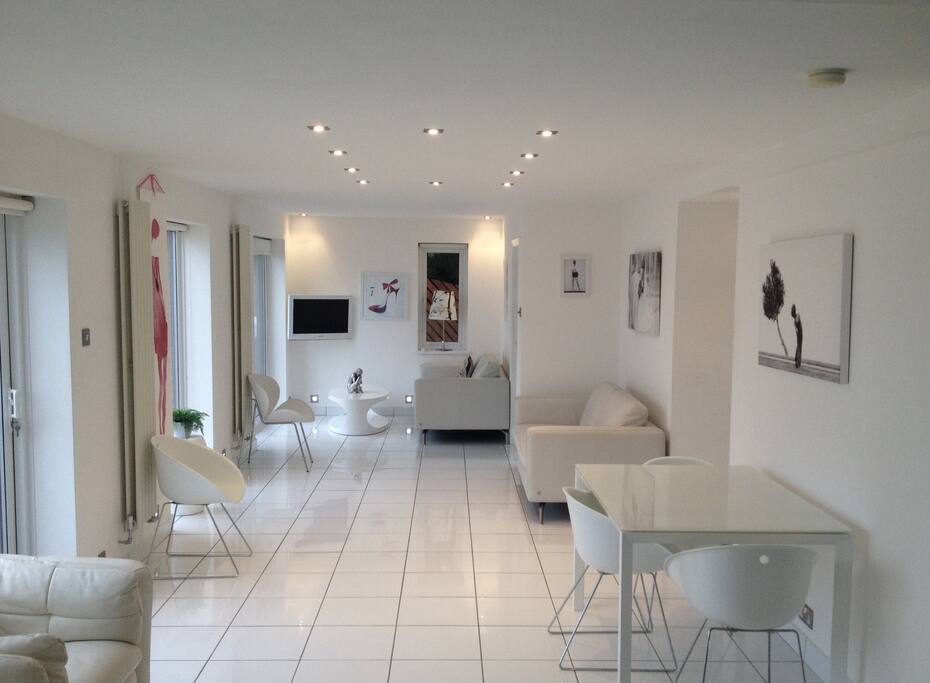 Rear facing white ceramic tiled modern living area with garden views through large patio windows and doors.