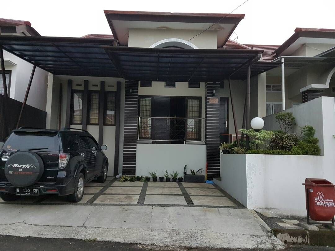 A well-maintained exterior features a covered carport shaded by a dark canopy. The front entrance, adorned with neatly arranged plants, leads to a welcoming doorway. A pathway lined with stone tiles is visible, contributing to the tidy curb appeal of the home.