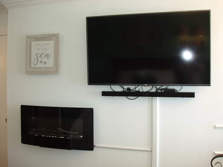 55hüvelykes LG TV hangszóróval és romantikus, tüzes fali kandallóval.