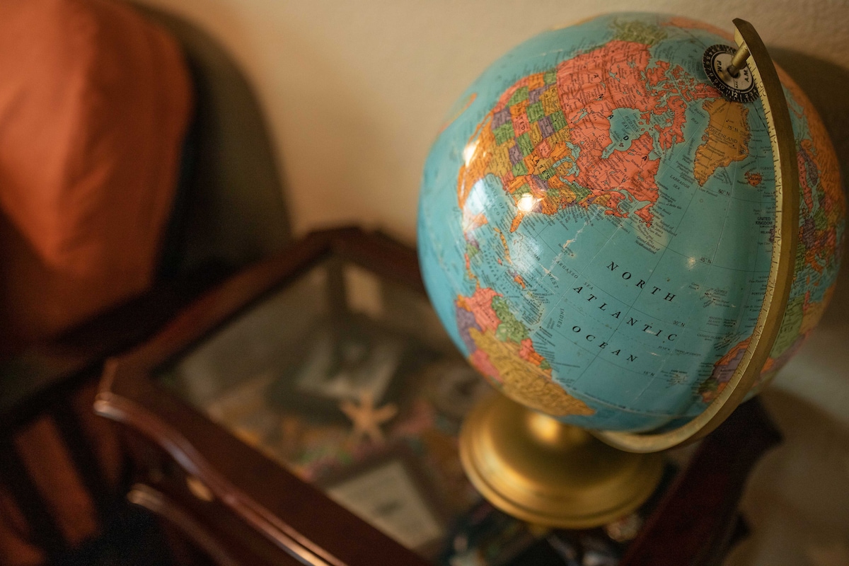 A vintage globe is displayed on a wooden side table. The globe features various colored continents and is oriented with the northern hemisphere facing upwards. Nearby, elements of travel-themed decor, including a starfish, are subtly arranged on the table.