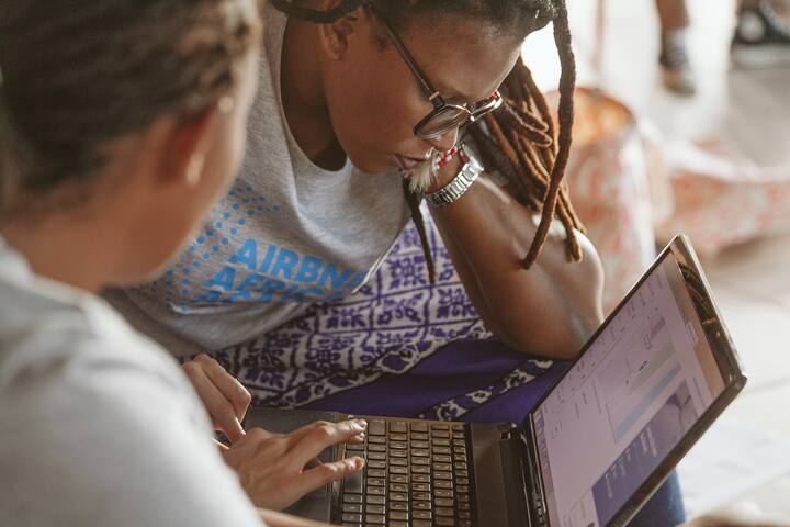 Two young women sit in front of a laptop screen while concentrating intensely