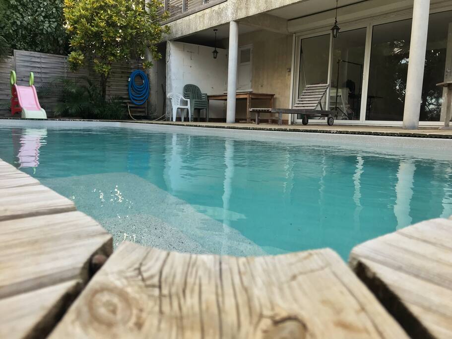 La piscine, le bas de la maison, table et chaises de jardin.