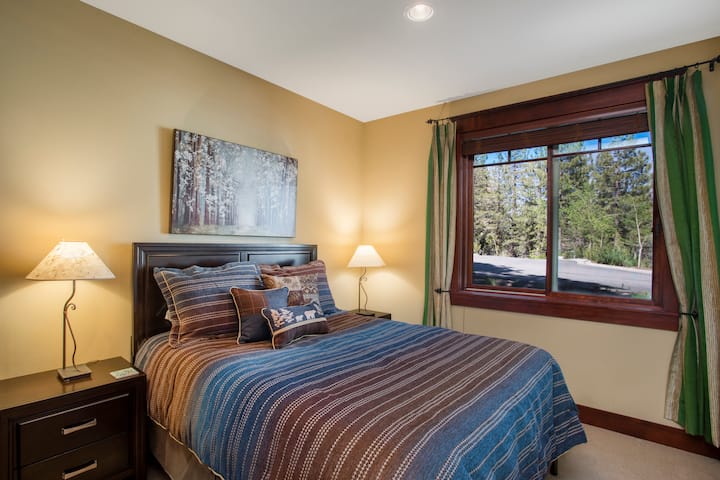 חדר השינה הנעים הזה בגודל קווין סייז כולל חלון גדול שמזמין הרבה אור טבעי, עם תאורה שקועה כדי ליצור אווירה חמה ומזמינה.